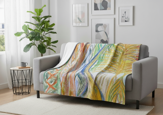 Scandi design living with two seater light gray couch,round coffee table with a cup of coffee and a book on it. There's a green leafy tall pot plant on the right side of the sofa, next to the white curtains. There're 4 abstract muted tone posters in white frames hanging on the wall behind the sofa. There's a light coloured textured rug under the sofa on a warm natural toned flooring.Divine Journeys of Healing Rainforest printed minky blanket laid on a couch showcasing the full multicolored design.